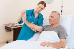 The nurse stands next to the old man and examines his hand.